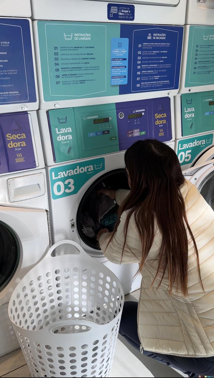 Cliente colocando roupas na lavadora profissional da A Gente Lava