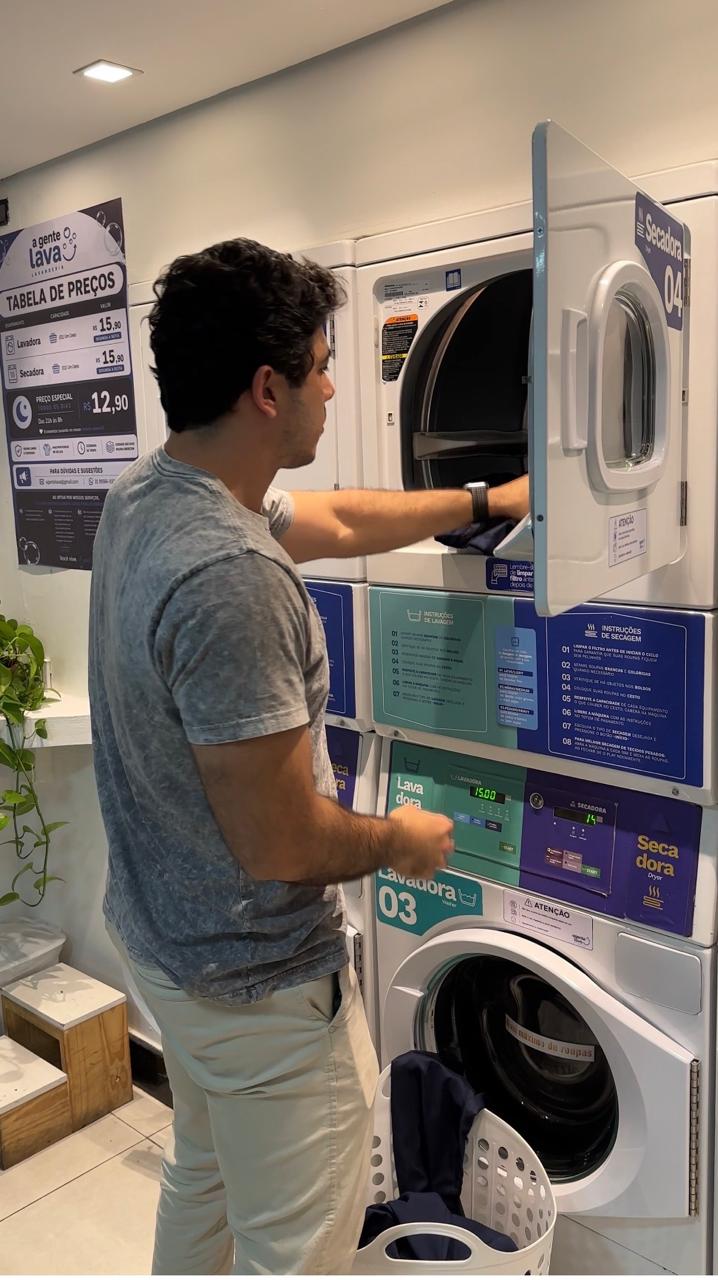 Cliente retirando roupas da secadora na lavanderia self-service A Gente Lava