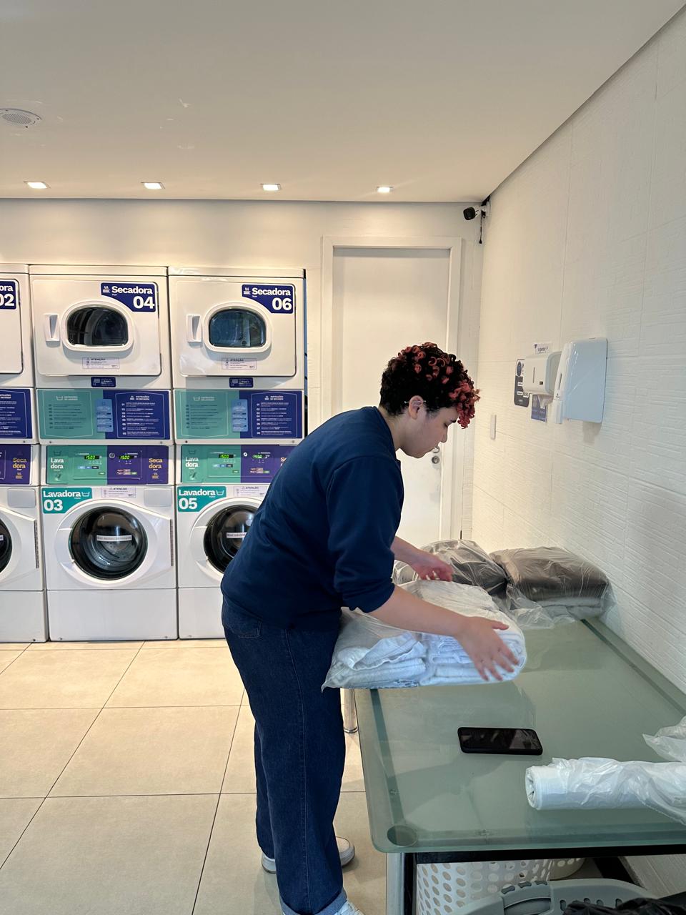 Colaboradora da A Gente Lava dobrando e embalando roupas na bancada da loja